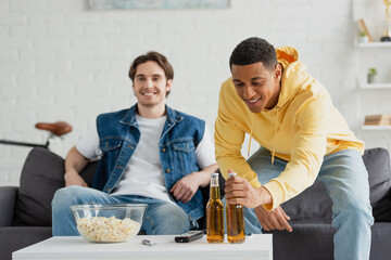 interracial friends resting with two bottles of beer and popcorn at home