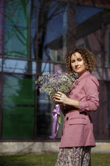 A slender stylish woman in lilac stands with a bouquet of gypsophila in the city.