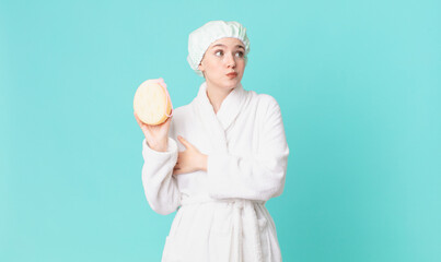 blond pretty woman shrugging, feeling confused and uncertain and wearing bathrobe