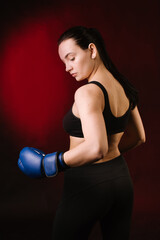 Strong sport woman boxer wearing blue boxing gloves on dark red background