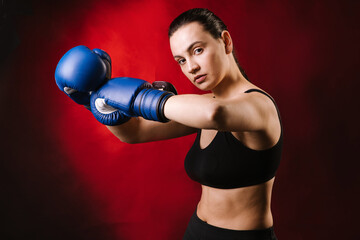 Strong sport woman boxer wearing blue boxing gloves on dark red background