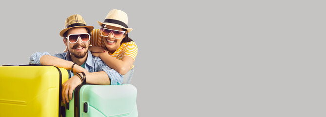 Travel on vacation concept. Happy smiling tourist in summer hat, sunglasses with suitcase luggage portrait studio shot with copy space over grey background. Advertising banner or poster design
