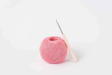 A ball of pink threads for knitting and a crochet hook on a white background.