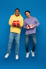 happy african american man with friend levitating with gift boxes in hands on blue background