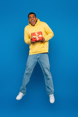 excited african american man levitating with red gift box on blue background