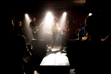 WIDE Punk rock band playing music during their concert on a stage of small venue. Vocals, guitars and drums. Shot with 2x anamorphic lens