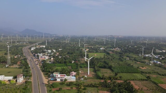 A landscape wide drone aerial moving shot of a two-lane busy roadway dividing huge farm of wind turbines on a bright sunny day in India. sustainable, clean, and renewable energy concept 