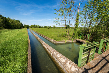 Fototapeta na wymiar Two small concrete irrigation canals in a rural scene, Padan Plain or Po valley (Pianura Padana, Italian). Mantua province, Italy, southern Europe.