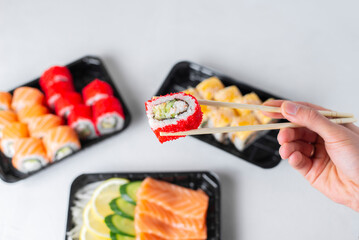 Man hands holding california roll with chopsticks. Lunch boxes, sushi set. Assorted rolls philadelphia, sashimi on light background. Restaurant delivery, takeaway concept. Japanese cuisine seafood