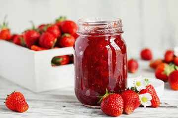 Homemade strawberry preserves or jam in a mason jar surrounded by fresh organic strawberries....