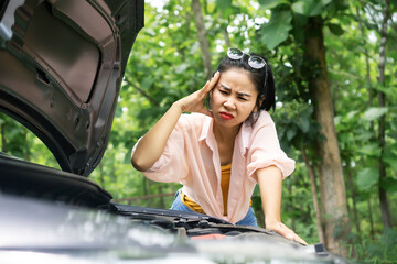 Asian woman having problem with broken car looking at opened  hood and try to check the engines feeling worry and upset 