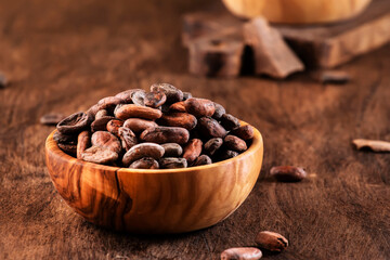 Unpeeled organic cocoa bean in bowl on wooden rustic table background. Copy space