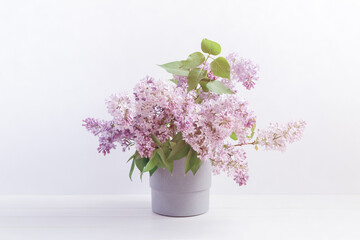 Floral layout with a bouquet of branches of blooming lilacs in a gray pot. Spring, summer template in pastel colors for banner, postcard, congratulations, social media.