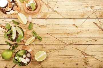 Fototapeta na wymiar Moscow mule alcoholic cocktail in copper mug with lime, ginger beer, vodka and mint. Wooden bar counter, bartender work tools, top view