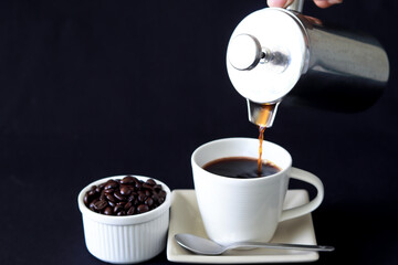 pouring coffee into coffee cup by French press coffee maker on black background with copy space