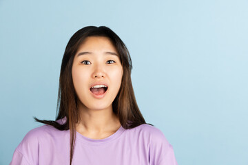 Asian young woman's portrait on blue studio background. Concept of human emotions, facial expression, youth, sales, ad.