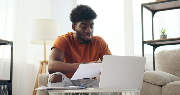 African American businessman reading document while doing video conference on laptop at home