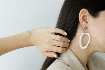 Stylish woman in beige suit with modern geometric earring posing and hand with white manicure holding beautiful hair. Beauty and hair care. Fashionable female with unusual glass accessories