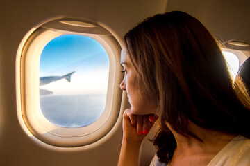 Young woman looking through window in airplane.Girl sitting in airplane near window. © ShoneNS