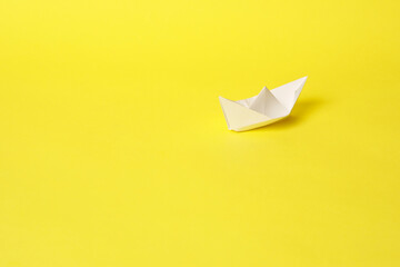A paper boat on a bright yellow background.
