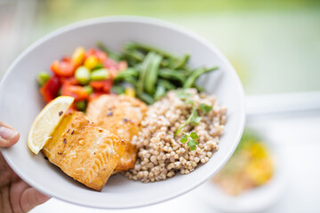 Hand holding salmon and buckwheat dish with green beans