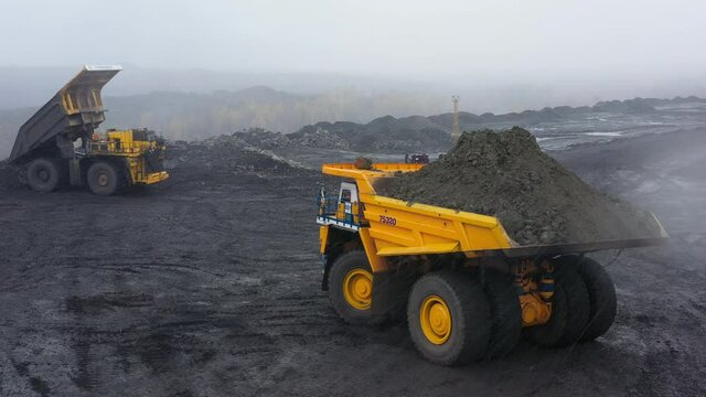 Large quarry dump trucks work at the coal mine in bad autumn weather. They drive on dirty roads. They are loaded with rock. The footage was taken on a quadrocopter.
