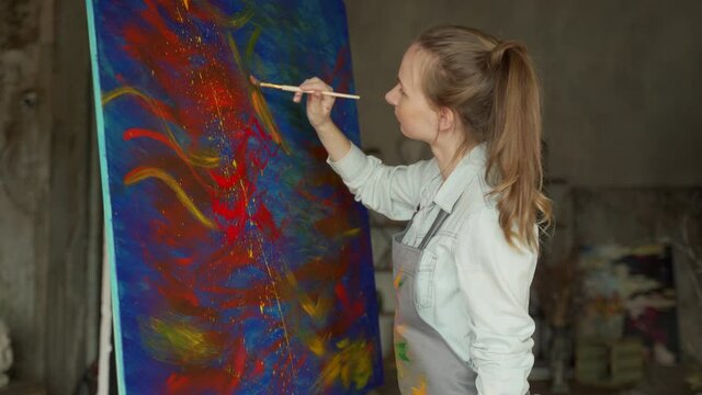 Female artist in front of an easel, painting with a brush, using oil or acrylic paint