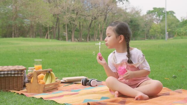 Happy little girl kid blowing soap bubbles playing alone in the park, Child having fun outdoor. Authentic happy childhood magic moment. Lifestyle seasonal activity for children.