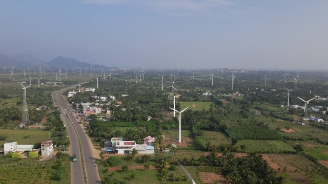 A landscape wide drone aerial moving shot of a two-lane busy roadway dividing huge farm of wind turbines on a bright sunny day in India. sustainable, clean, and renewable energy concept 