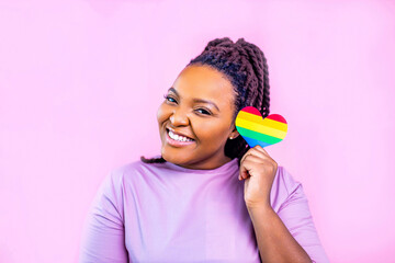 Portrait of an attractive hispanic woman holding a LGBT rainbow heart in pink studio