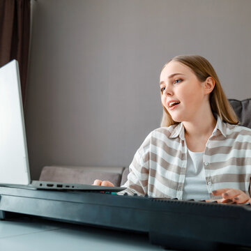 Woman learns music singing vocals playing piano online using laptop at home interior. Teenager girl sings song play piano synthesizer during video call, online lesson with teacher. Closeup portrait.