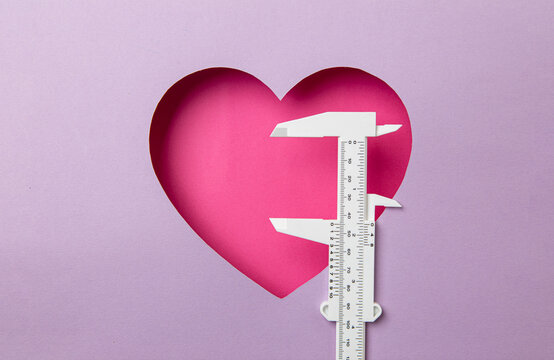 Pink heart on a purple background. At the heart is a white micro meter. Concept measuring love.