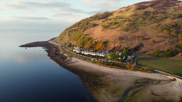Aerial view of the Scottish town of Catacol on the Isle of Arran at sunset, Scotland. Moving away from town over the sea whilst elevating.