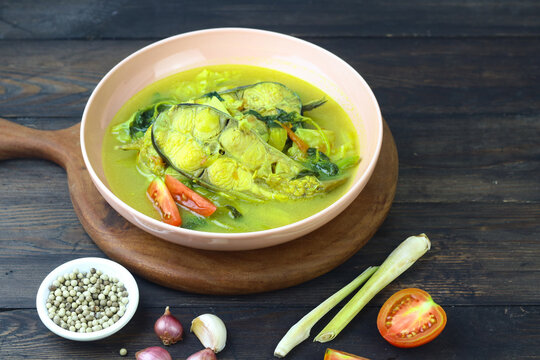 Pindang Ikan Patin or Catfish vegetables Soup , Indonesian food popular from Palembang. Served on ceramic bowl garnished wit tomato slices. Copy space for text. Dark wooden background. 