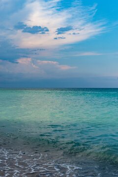 Beautiful seascape, green and turquoise tones and shades on flat sea water surface, blue sky, grey pink clouds before storm at sunset evening time. Natural colorful pattern background, vertical frame.