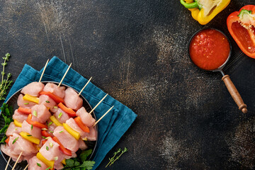 Raw shish kebab on wooden board, spices, herbs and vegetables on dark grey background. Barbecue Raw...