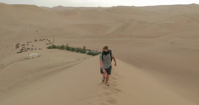 Man walking on desert dunes, oasis background cloudy day