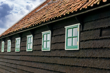 close up of the tarred wooden siding of a traditional Dutch farmhouse with many small green windows