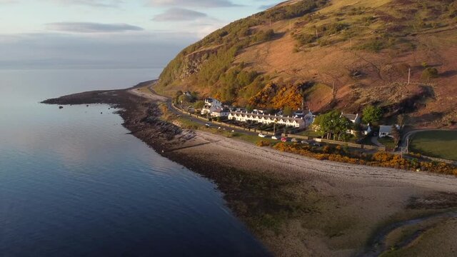 Aerial view of the Scottish town of Catacol on the Isle of Arran at sunset, Scotland. Right to left view flying away from the town with slow zoom in.