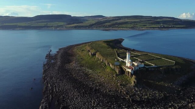 Aerial view of Pladda Lighthouse on the Isle of Arran on a sunny day, Scotland. Flying away from the lighthouse with the Isle of Arran behind.