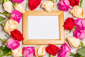 Multicolored fresh roses and a wooden frame on light stone background