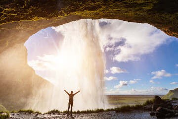 Happy female traveler feeling the power of Seljalandsfoss waterfall in the South of Iceland, person...