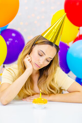 Woman with candles on a birthday cake on a background of gifts and balloons