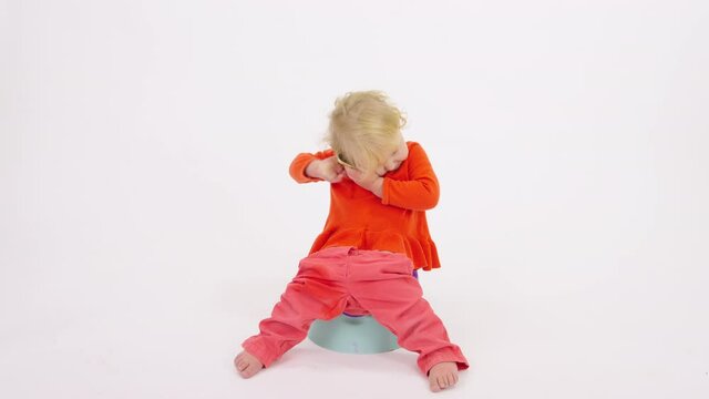 Adorable toddler girl sitting on potty talking on her smartphone and amusingly dropping it from hands isolated on white studio. smart kid learns Internet technology. Getting baby accustomed to potty