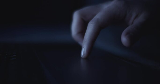 Close up of a finger using a laptop touchpad to browse the internet at night. Slow motion, shallow depth of field. 
