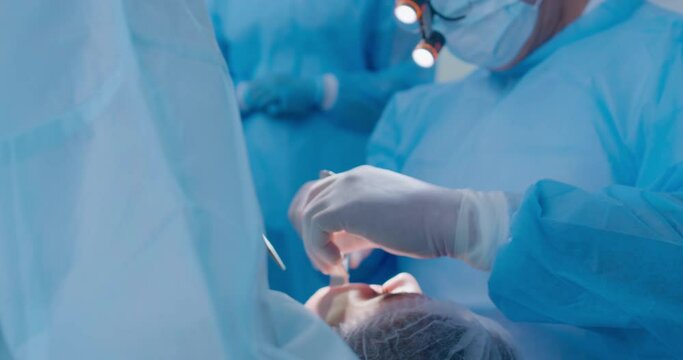 Close-up a male dentist with shadowless headlamp on the head and disposable mask is doing teeth treatment to the female patient by using dental forceps and taking out a pulled-out tooth from the mouth
