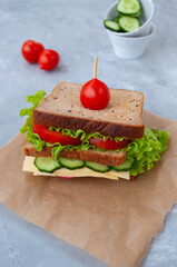 Delicious sandwich with fresh lettuce leaves, tomatoes, cucumbers and cheese on a grey table background.