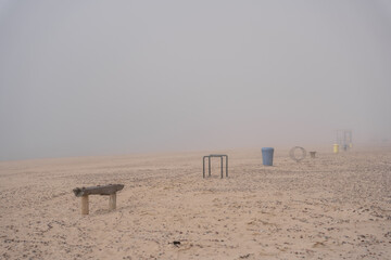 Fototapeta na wymiar The beach of the Baltic Sea in Ventspils, where there is a thick fog, you can only see benches and rubbish bins placed in the sea sand