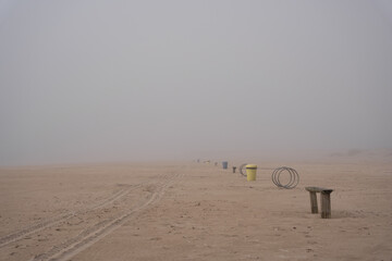 Fototapeta na wymiar Baltic Sea beach in Ventspils covered with thick fog, garbage cans and benches in the distance