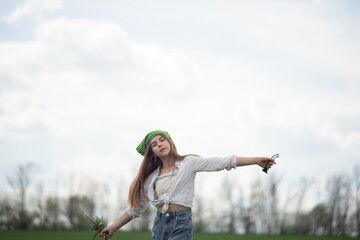 fashionable little girl in denim style in a green field, against the backdrop of a cloudy sky